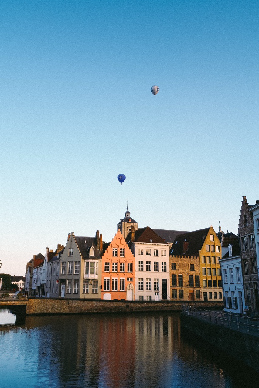 historische gevels langs een kanaal in west-vlaanderen met hete luchtballonnen van Airo aan de heldere blauwe hemel