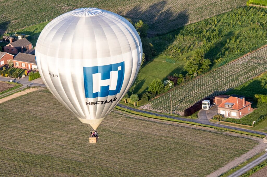 ballonvaart met hectaar logo boven landelijke velden verzorgd door Airo in West-Vlaanderen en Henegouwen