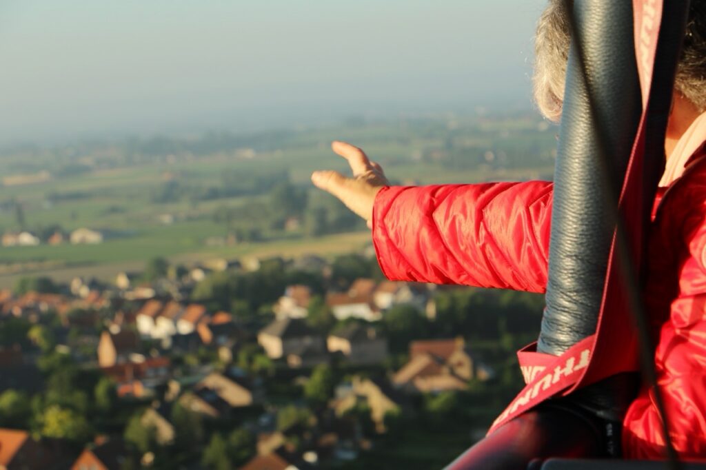 passagier in rode jas geniet vanaf hoge luchtballon van uitzicht op dorp en groene velden airo ballonvaarten