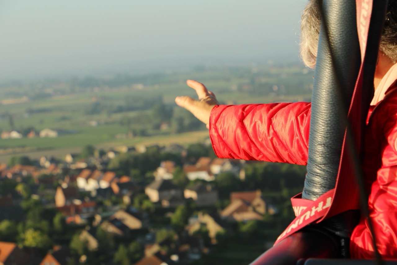 passagier in rode jas geniet vanaf hoge luchtballon van uitzicht op dorp en groene velden airo ballonvaarten